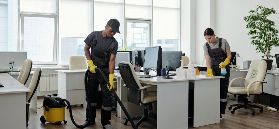 young-black-man-workwear-cleaning-floor-while-girl-wiping-desks-with-computers